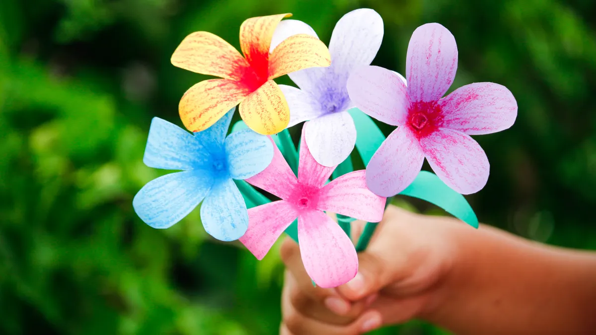 Hand holding pastel paper flowers outdoors