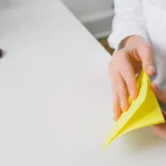 Person folding yellow origami paper at a desk