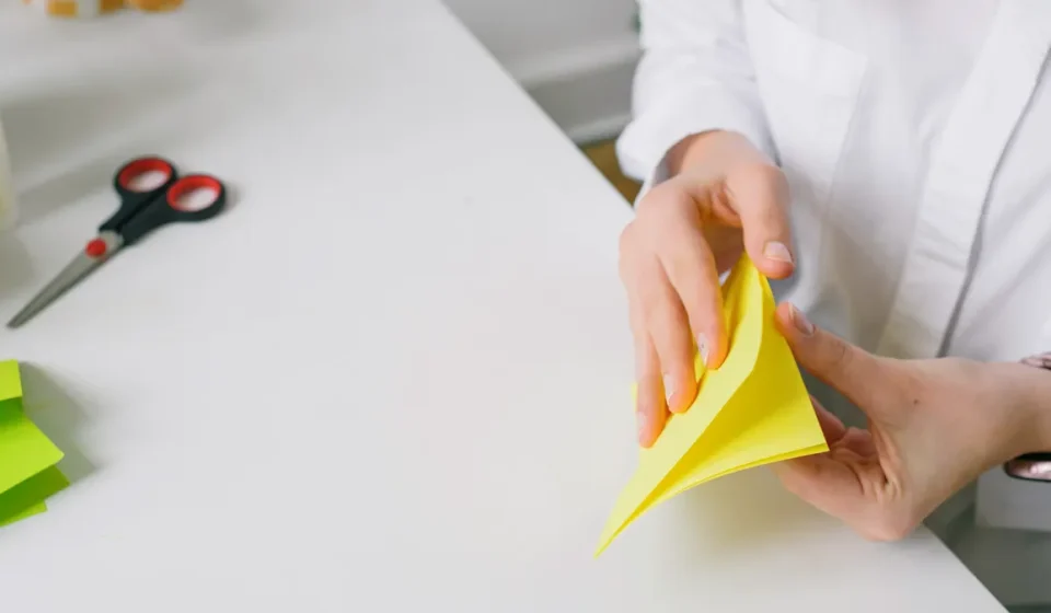 Person folding yellow origami paper at a desk