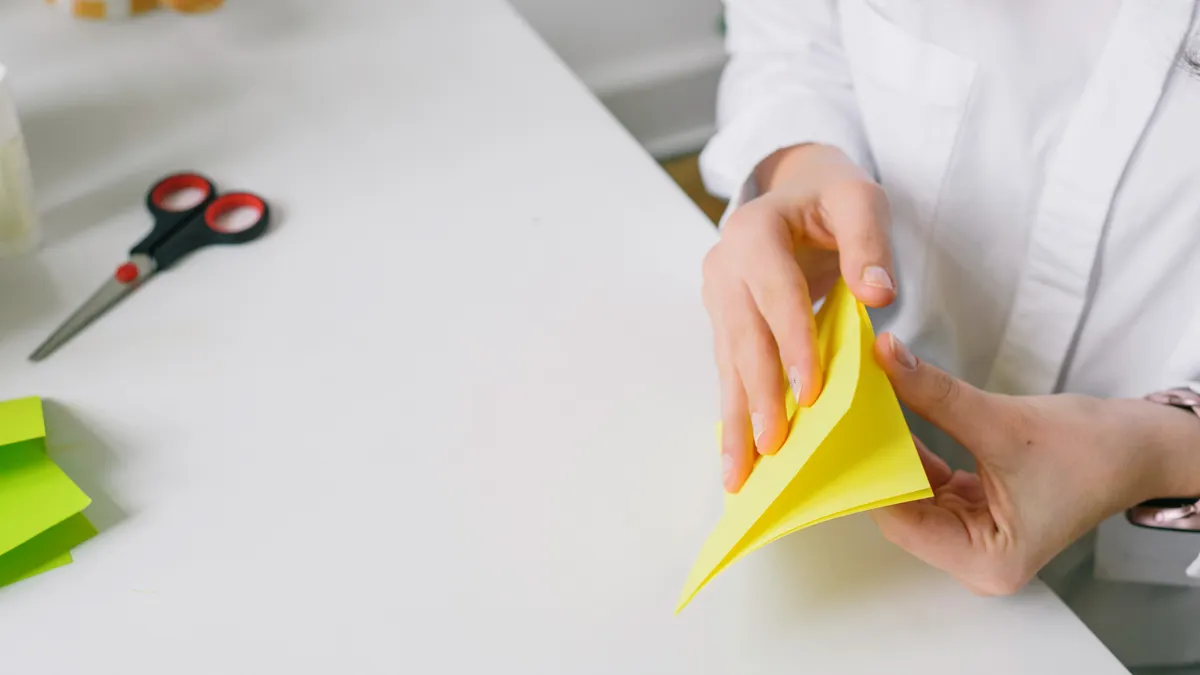Person folding yellow origami paper at a desk
