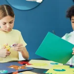 Children cutting and gluing colorful paper crafts at a table