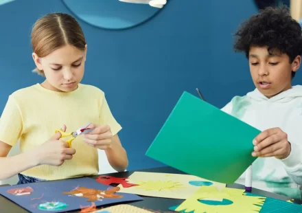 Children cutting and gluing colorful paper crafts at a table