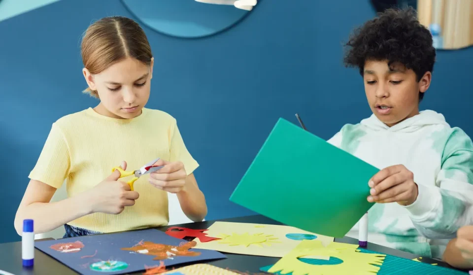 Children cutting and gluing colorful paper crafts at a table